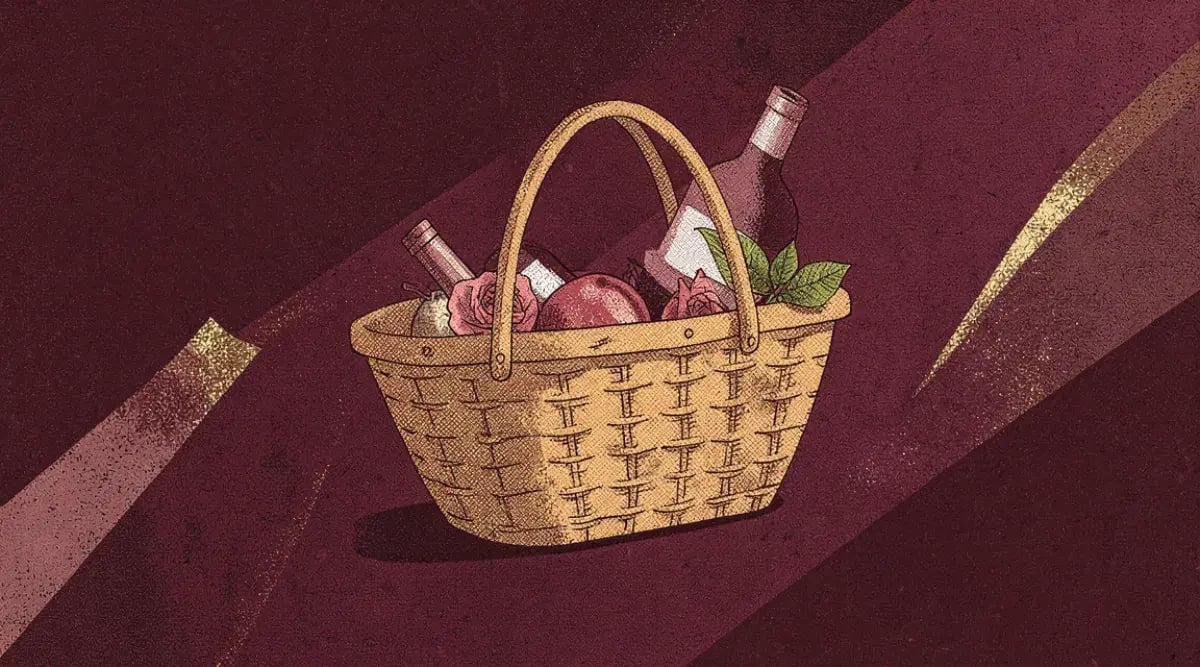 Botella de vino rosado junto a canasta de picnic con quesos y frutas al aire libre