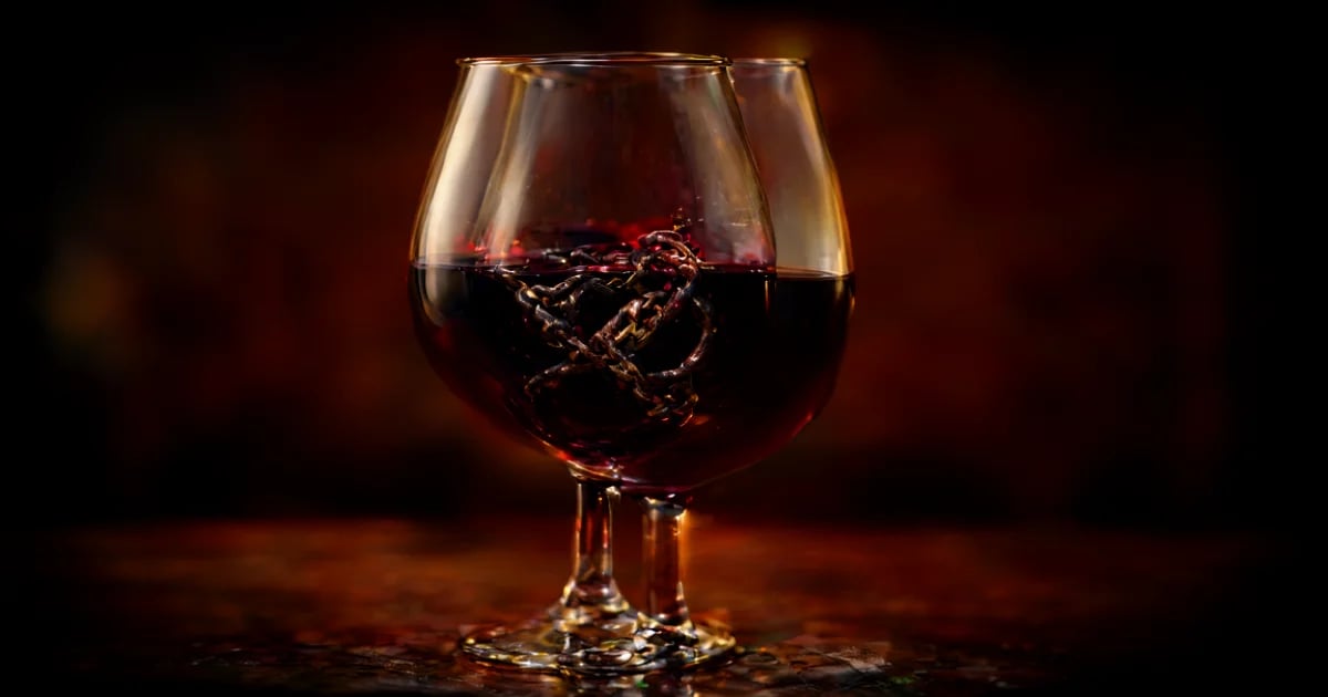 Copa de vino Tannat con color rojo oscuro casi negro y viñedos uruguayos al fondo